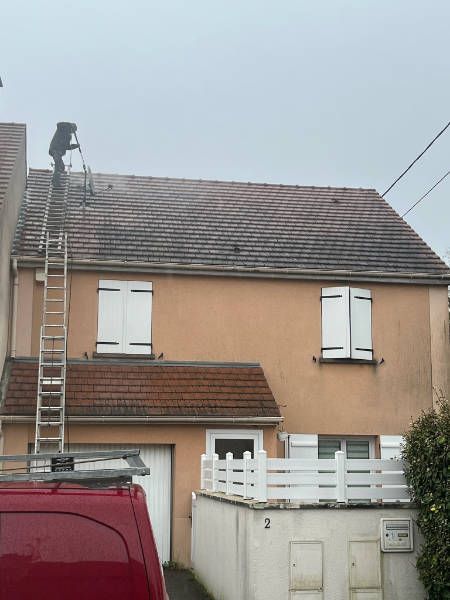 Monsieur Moïse, Fortin, sur une toiture équipée d'échelle de toiture en train d'appliquer un jet haute pression pour retirer les mousses sur un toit à Rambouillet dans les Yvelines